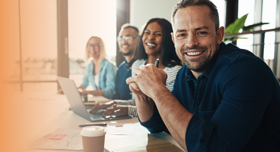 Mental health at work: Four employees of a company sit together in a meeting, with laptops, notebooks and cups of coffee on the table in front of them